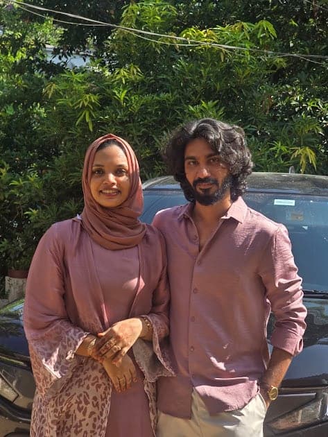 Fazna in a rose abaya and headscarf and Nisham in a rose shirt, under green trees