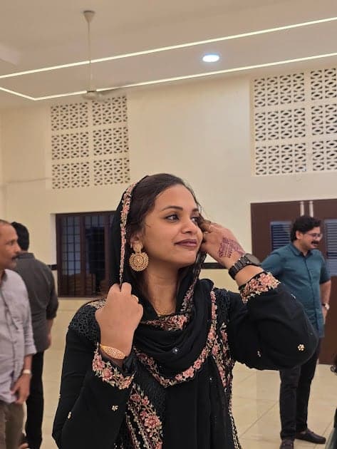 Fazna in a black embroidered dress, adjusting her earring