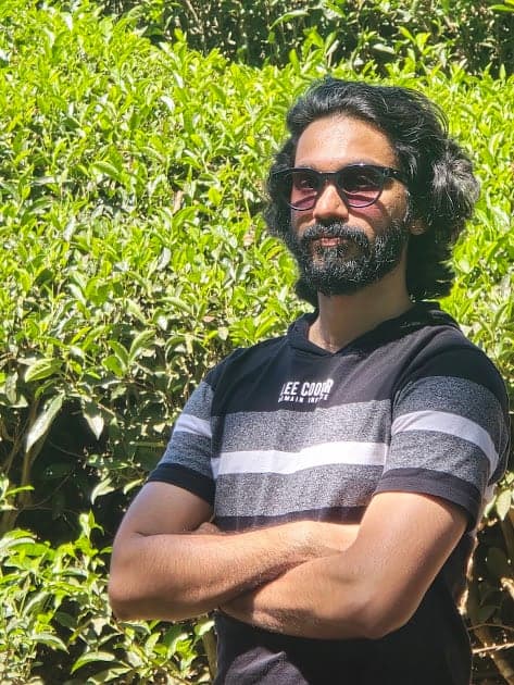 Nisham in sunglasses with arms crossed among trees
