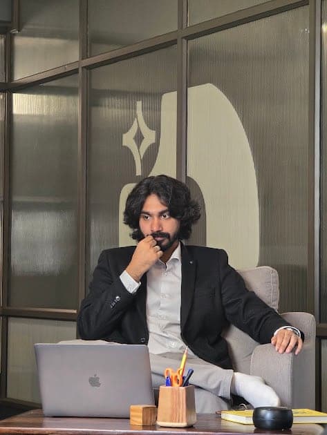 Nisham at a desk with a laptop, in a dark blazer