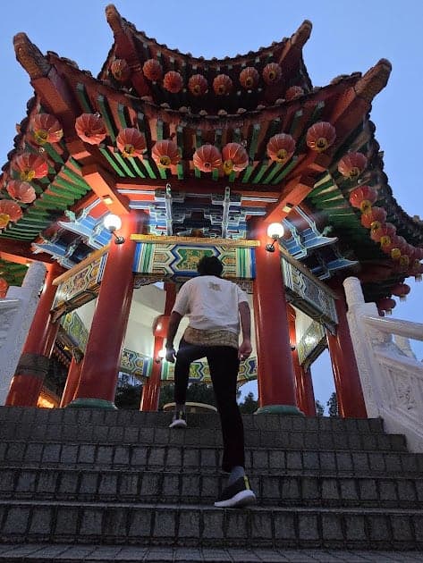 Nisham on the steps of a red and gold temple gate